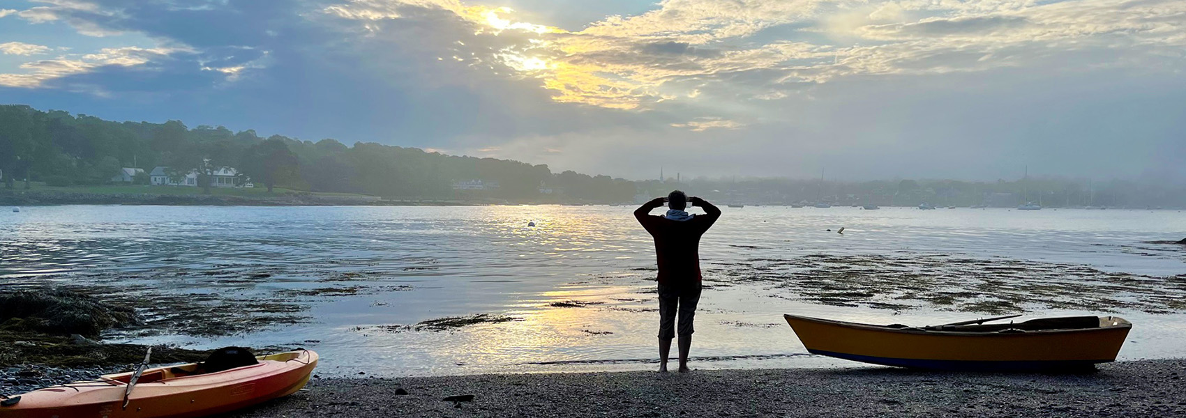 person on beach near boats looking at sun